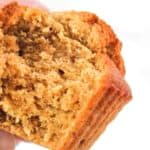 A person holds a partially eaten, golden-brown muffin, showcasing its fluffy and moist texture.