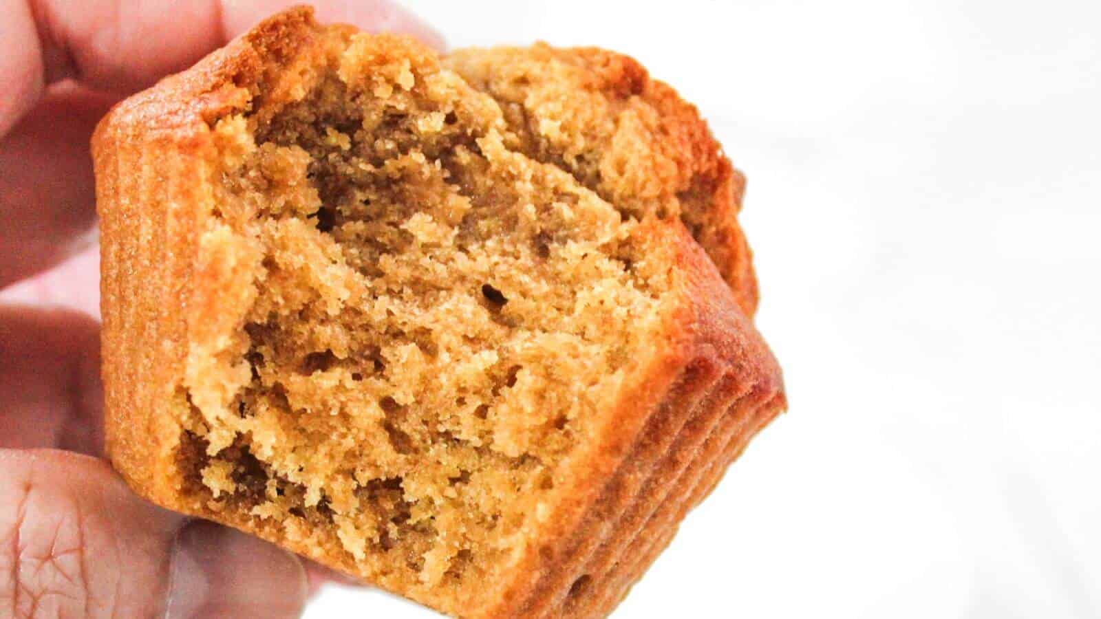 A person holds a partially eaten, golden-brown muffin, showcasing its fluffy and moist texture.