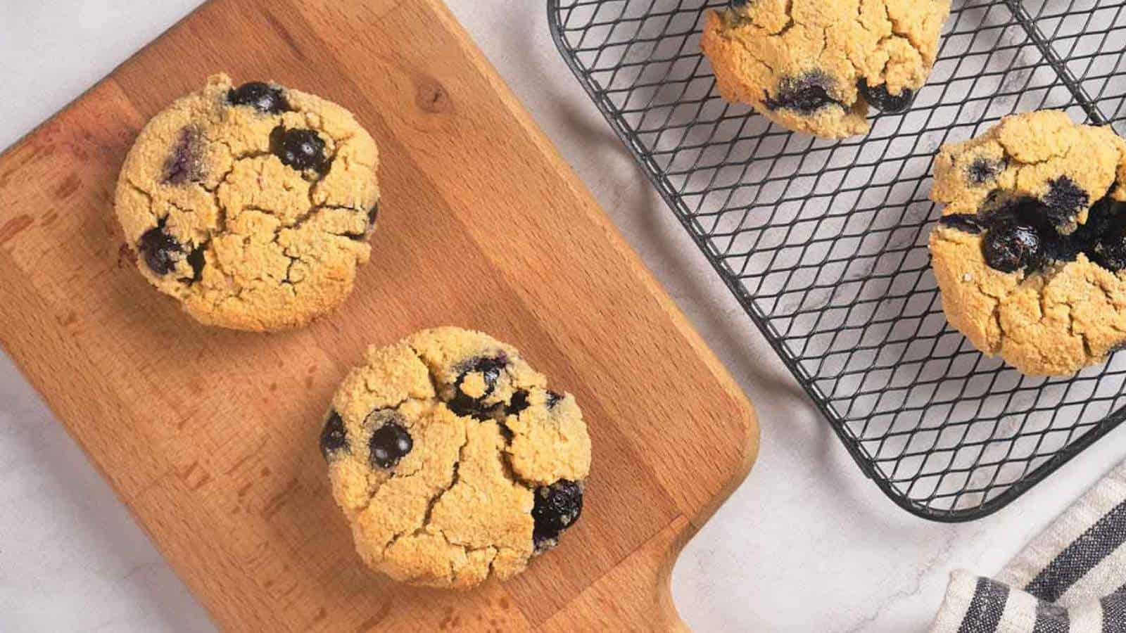 Four blueberry scones, some on a wooden cutting board and others on a cooling rack.