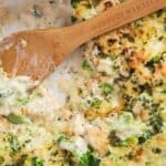 A wooden spoon scooping chicken broccoli Alfredo casserole out of a serving dish.