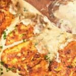Pan with four browned chicken breasts in a creamy sauce, garnished.