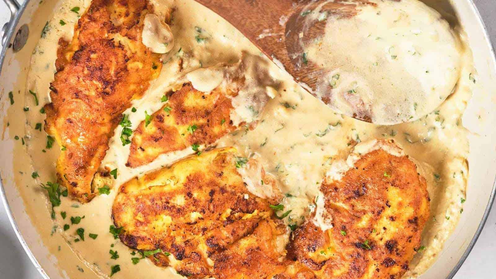 Pan with four browned chicken breasts in a creamy sauce, garnished.