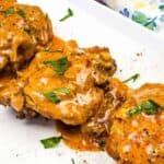 Three pieces of chicken smothered in a creamy, orange-hued sauce topped with chopped herbs, served on a white rectangular plate.
