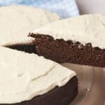 A slice of chocolate cake with white frosting being lifted from the whole cake.