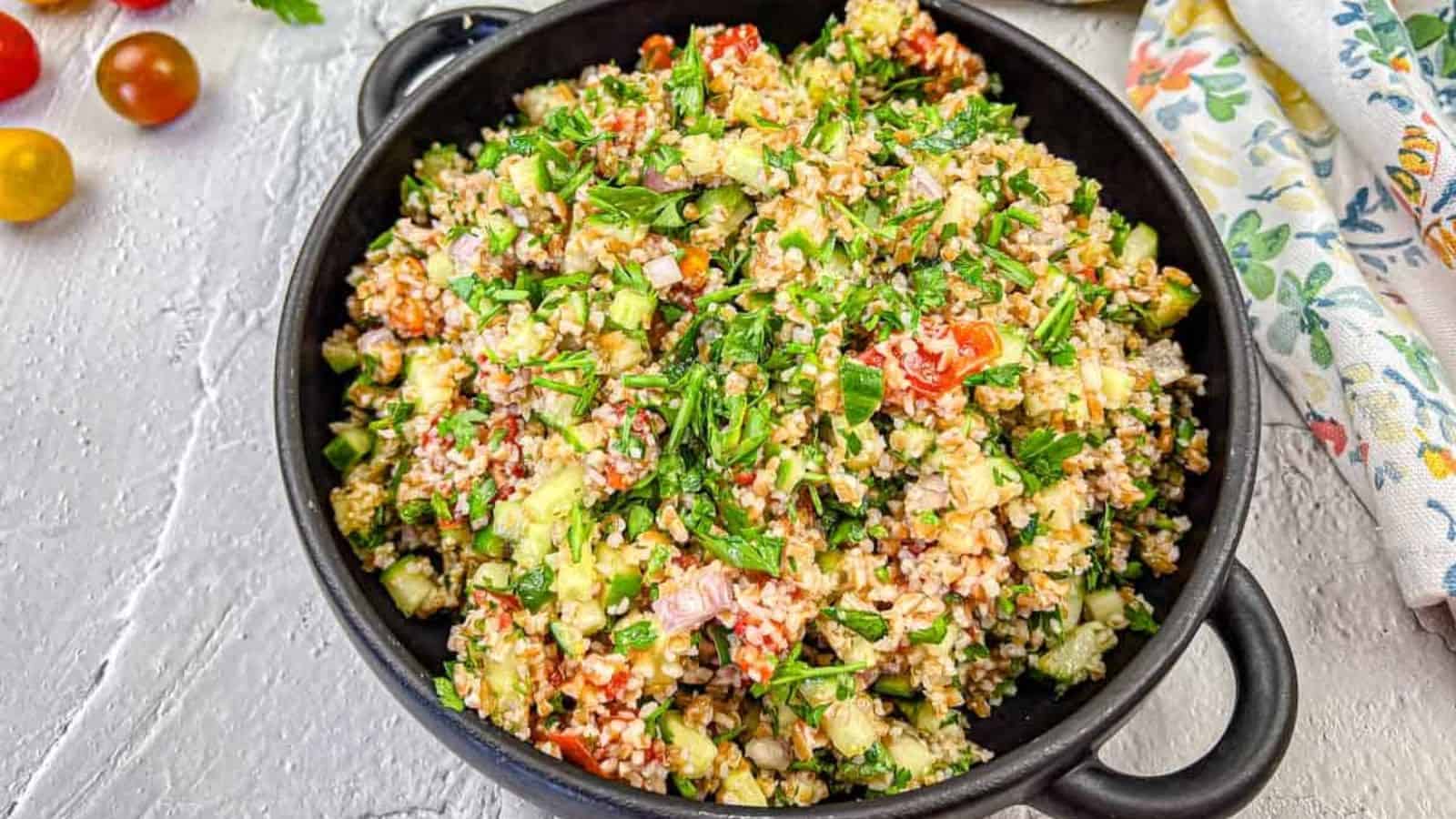 A black bowl filled with tabbouleh salad with smoked tomatoes.