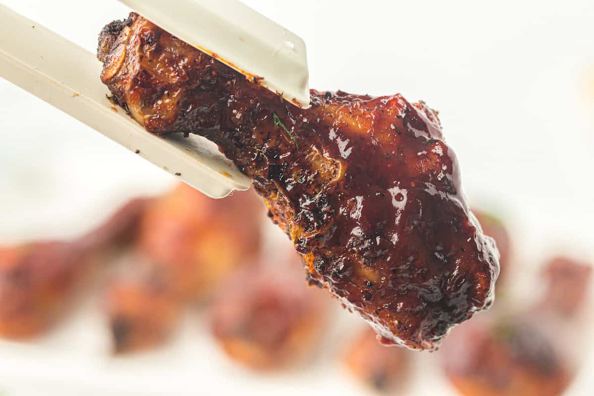 A close-up of chopsticks holding a piece of glazed, grilled chicken. The chicken appears juicy and well-cooked.