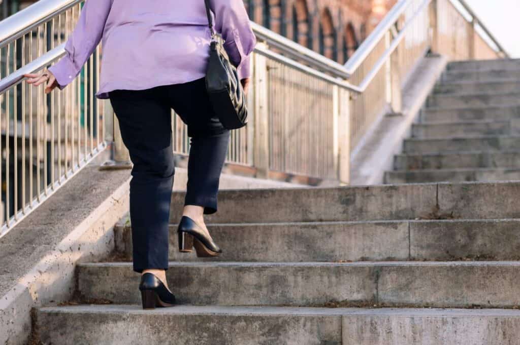 A woman in heels is walking up a concrete outdoor staircase.