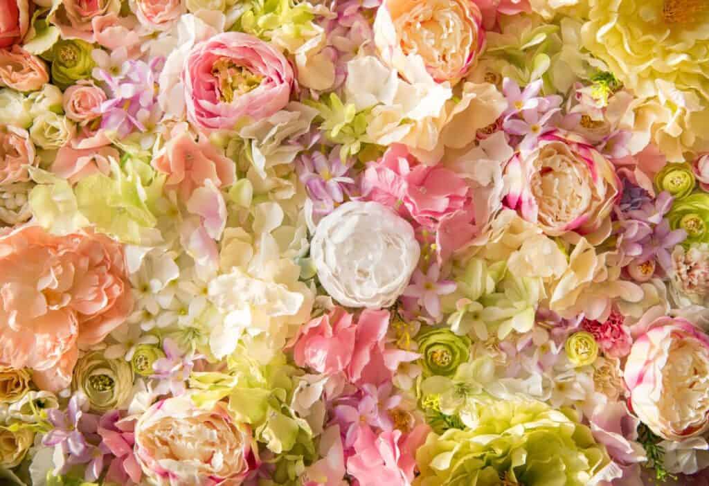 A variety of pastel-colored types of flowers, including roses, peonies, and hydrangeas, are densely arranged, creating a vibrant floral background.