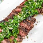 A plate of sliced grilled steak topped with a green herb sauce, served on a white rectangular dish.