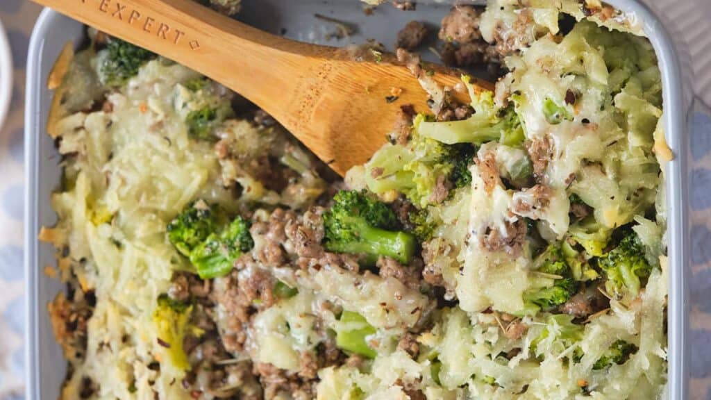 A baked casserole dish with ground beef and broccoli casserole and a wooden spoon.