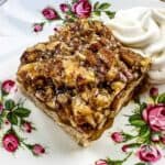 A slice of maple pecan pie bar topped with chopped pecans sits on a floral-patterned plate.