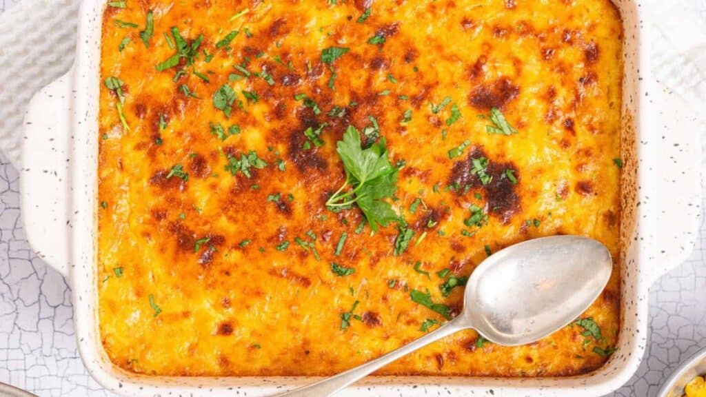 A baked casserole with a browned cheese crust topped with chopped parsley, served in a rectangular dish with a spoon on the side.