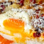 Close-up of a slice of pizza topped with a runny fried egg, grated cheese, bacon bits, and black pepper.