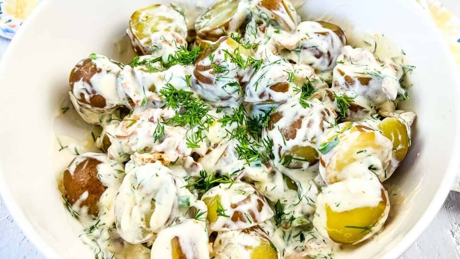 A bowl of boiled potatoes with skins on, topped with a creamy herb sauce and garnished with chopped fresh dill.