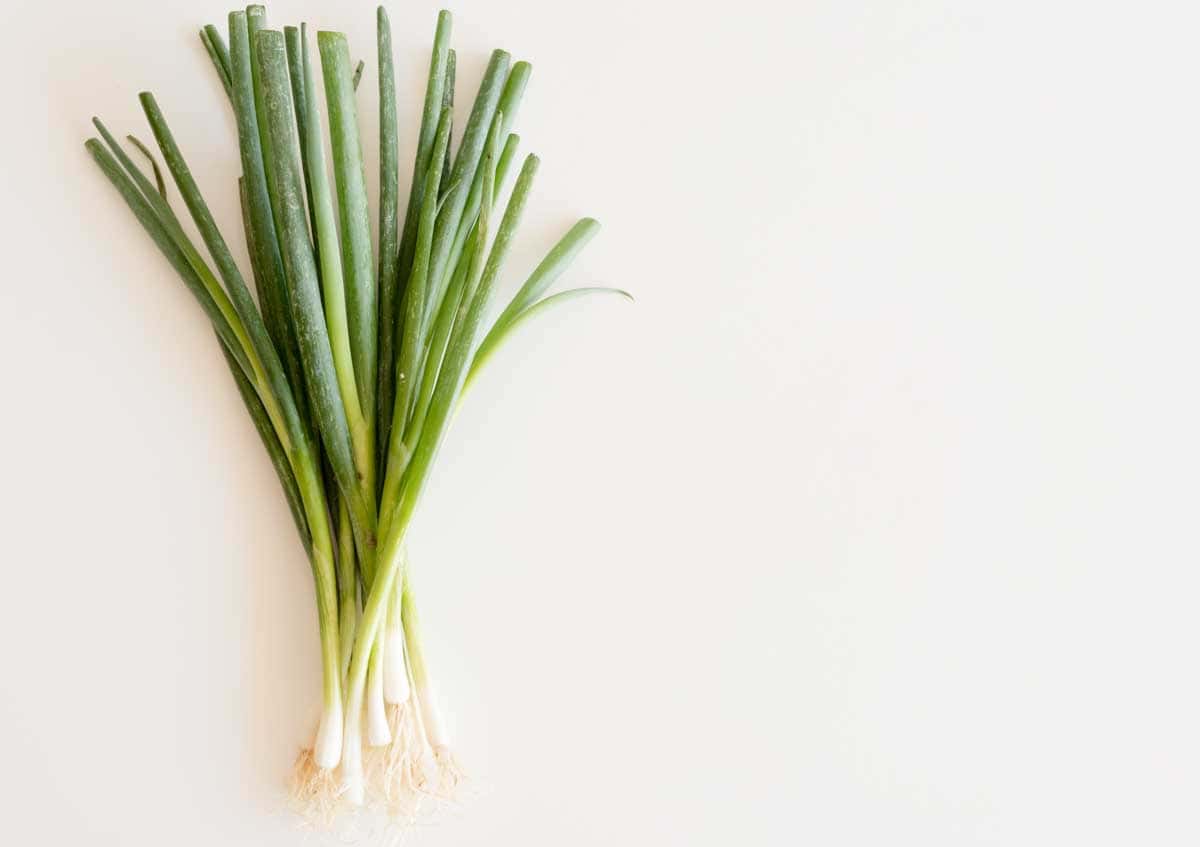 A bunch of green onions with white roots on a light background.