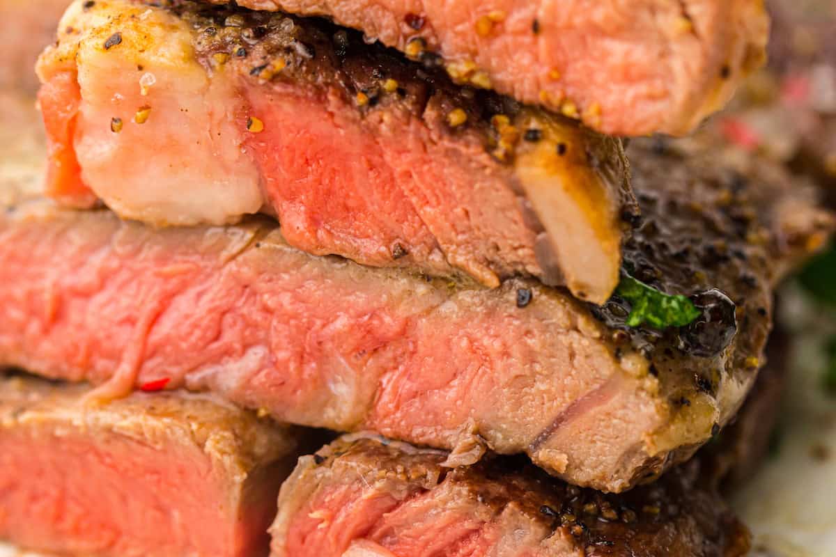 Close-up of a stack of medium-rare, seasoned steak slices, showcasing a pink and juicy interior with a seared crust.