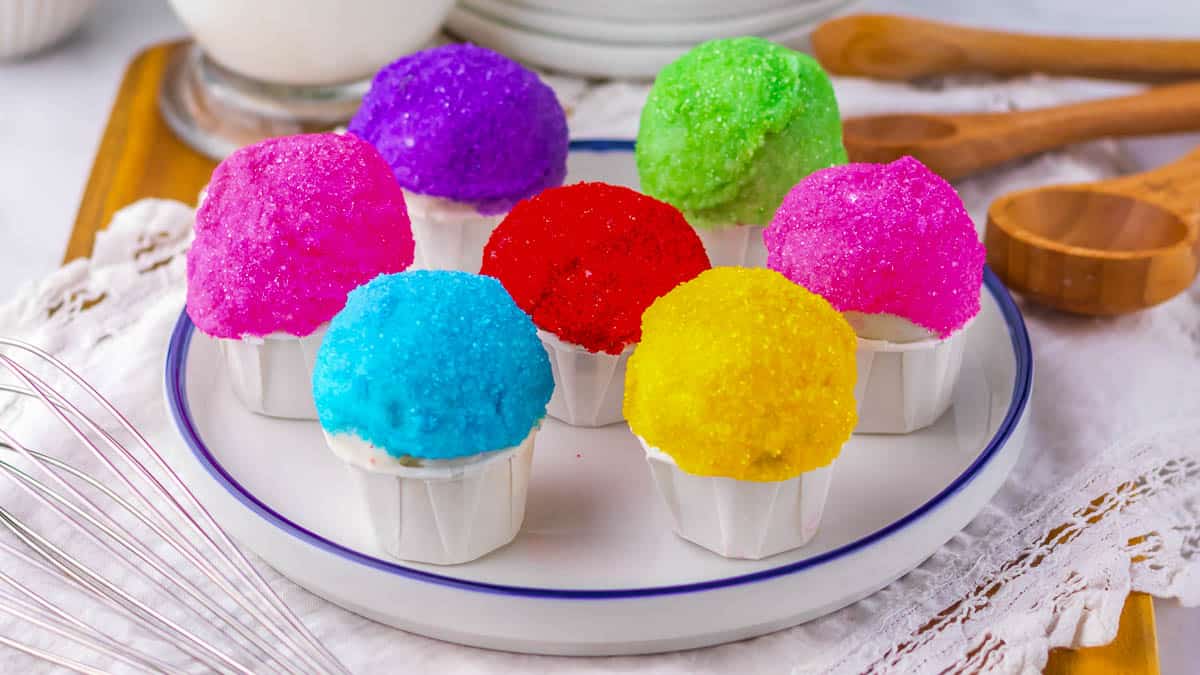 A plate with seven snowcone oreo balls topped with brightly colored sugar crystals sits on a table.