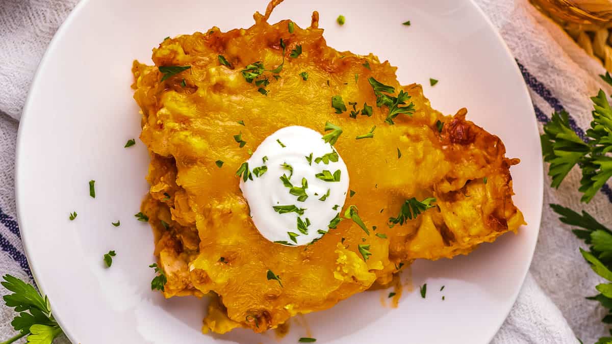 A plate of chicken tamale pie casserole topped with a dollop of sour cream, garnished with chopped parsley, on a white plate.