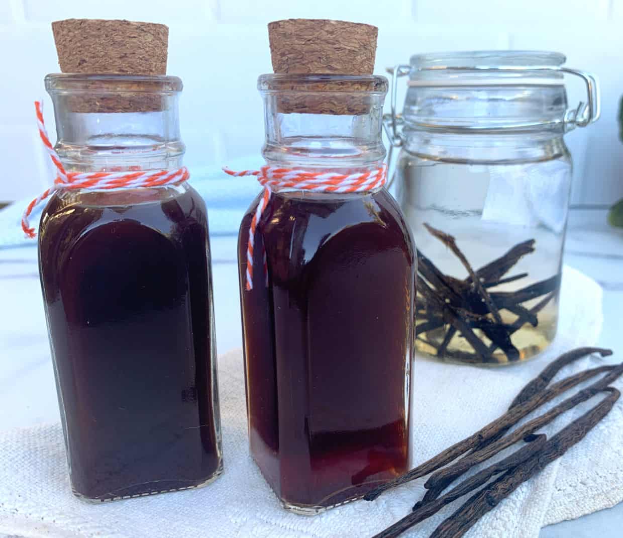 Two glass bottles filled with dark vanilla extract and several loose vanilla beans.