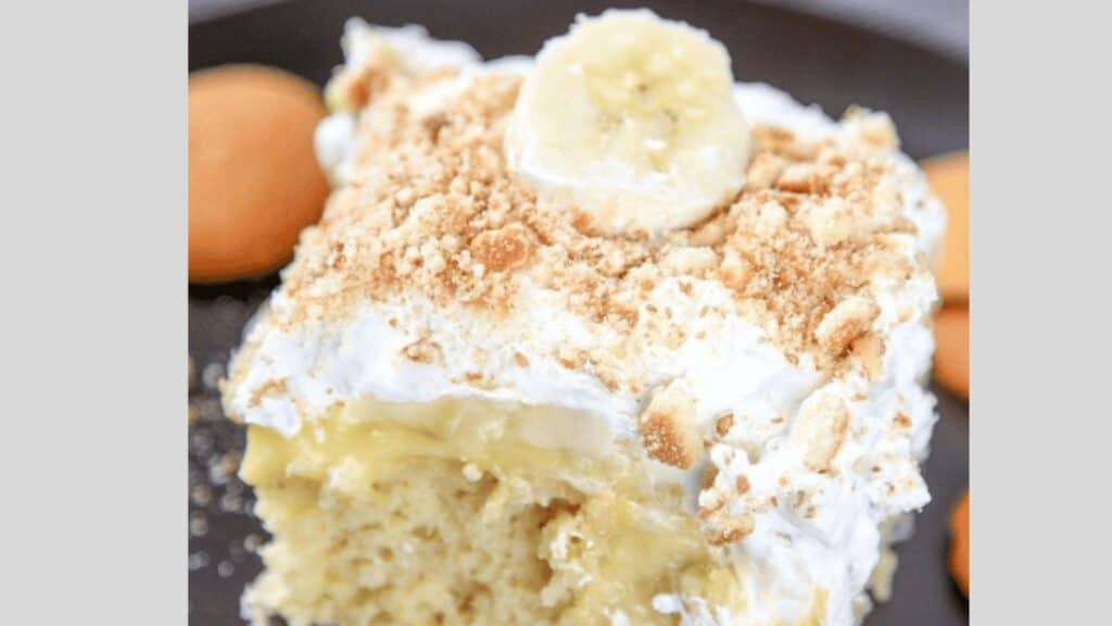 A close-up of a slice of banana pudding dessert topped with a banana slice and crushed cookies.