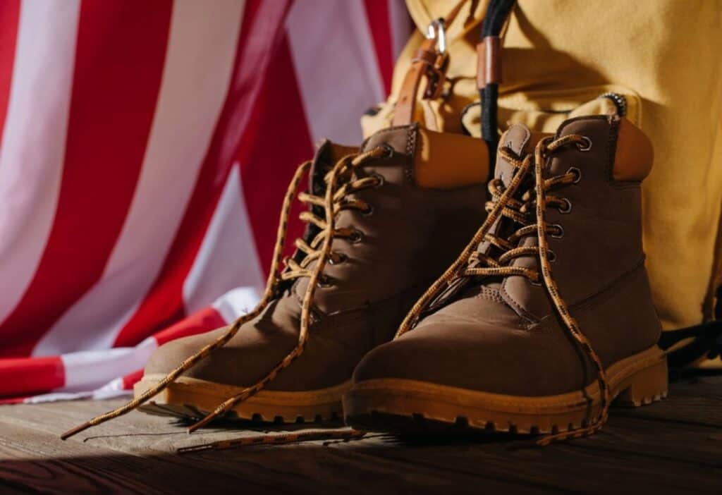 A pair of brown hiking boots with yellow laces next to a yellow backpack, set against a backdrop of a red and white striped fabric.