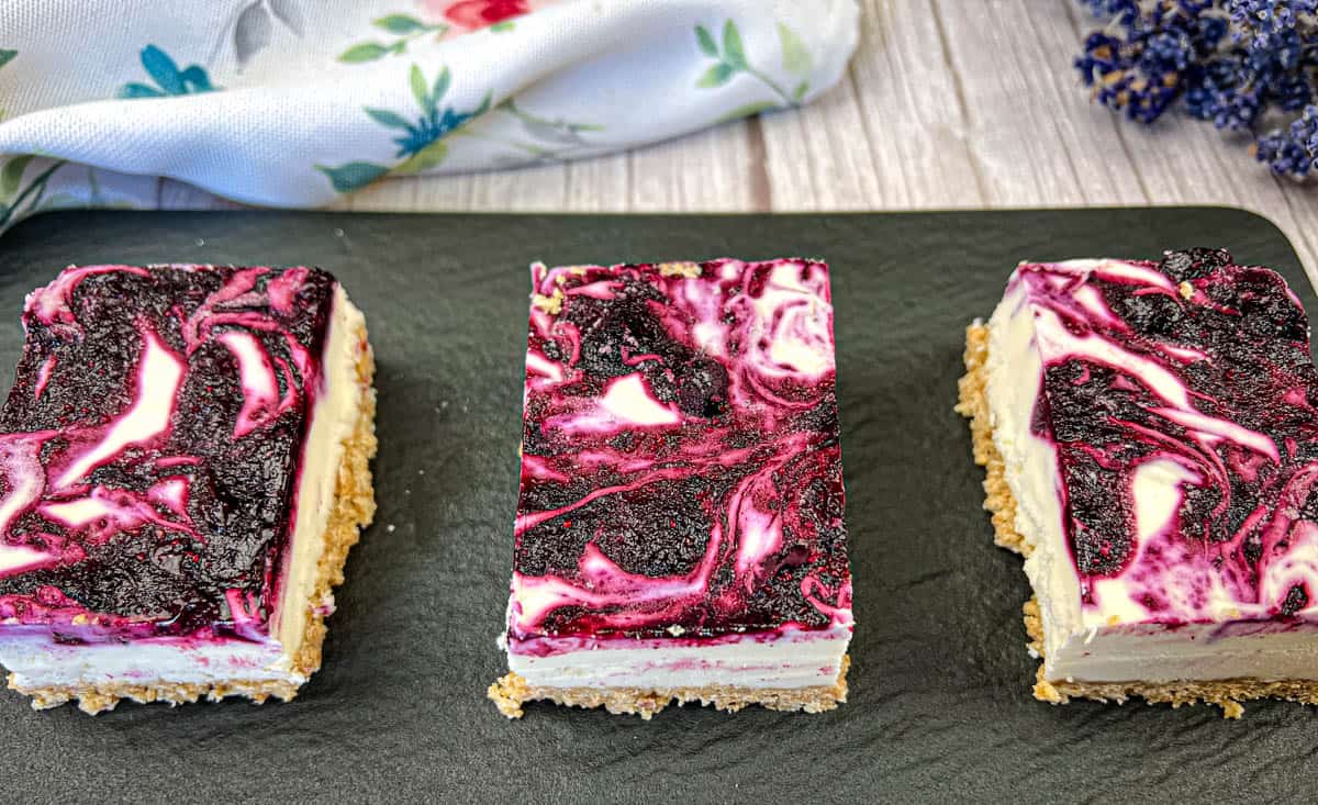 Three pieces of No-Bake Blueberry Cheesecake Bars on a black slate plate.