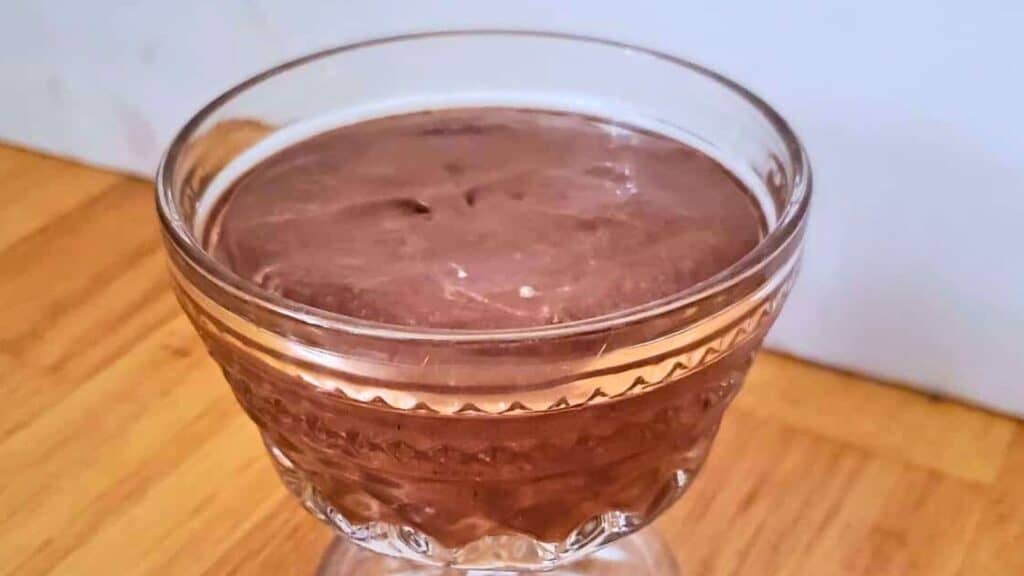 Image shows A glass bowl filled with chocolate mousse, placed on a wooden surface.