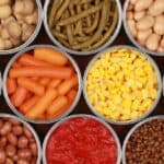 Assorted canned vegetables, including mushrooms, green beans, white beans, kidney beans, baby carrots, corn, peas, pinto beans, diced tomatoes, and lentils arranged in open cans—perfect for whipping up delicious dinners with quality canned goods.