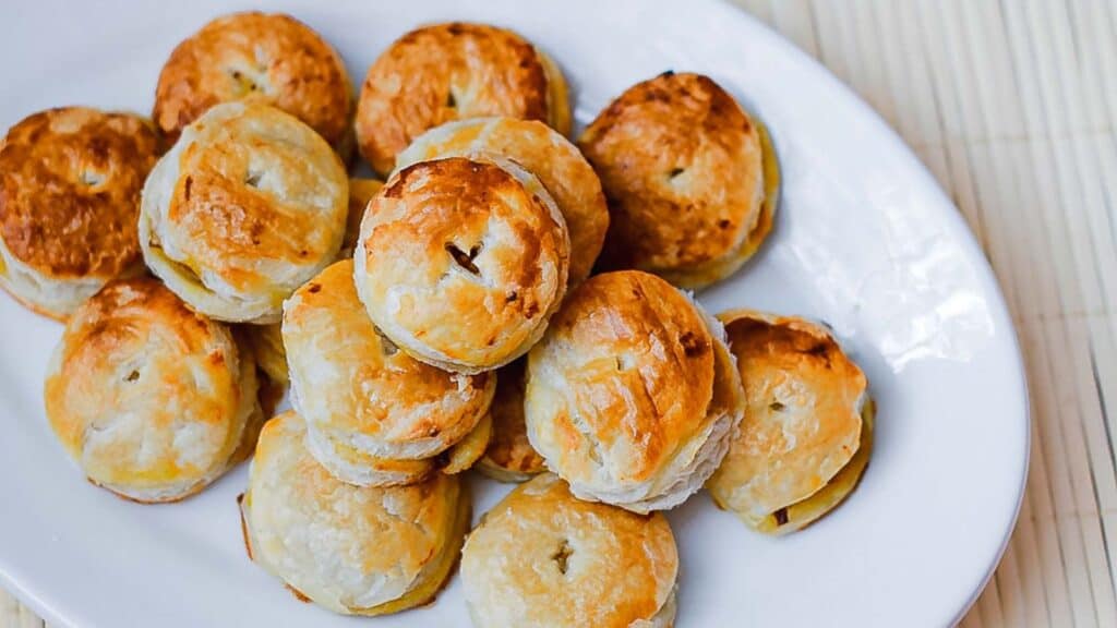 A white plate filled with a stack of small golden-brown puff pastries.