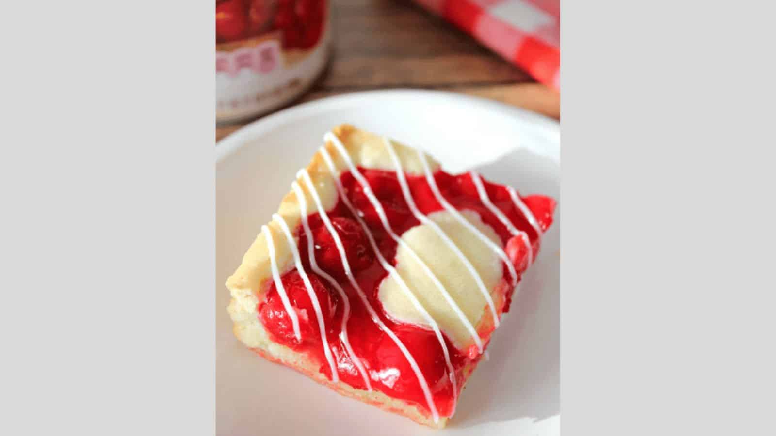 A square cherry pie bar drizzled with a vanilla glaze.