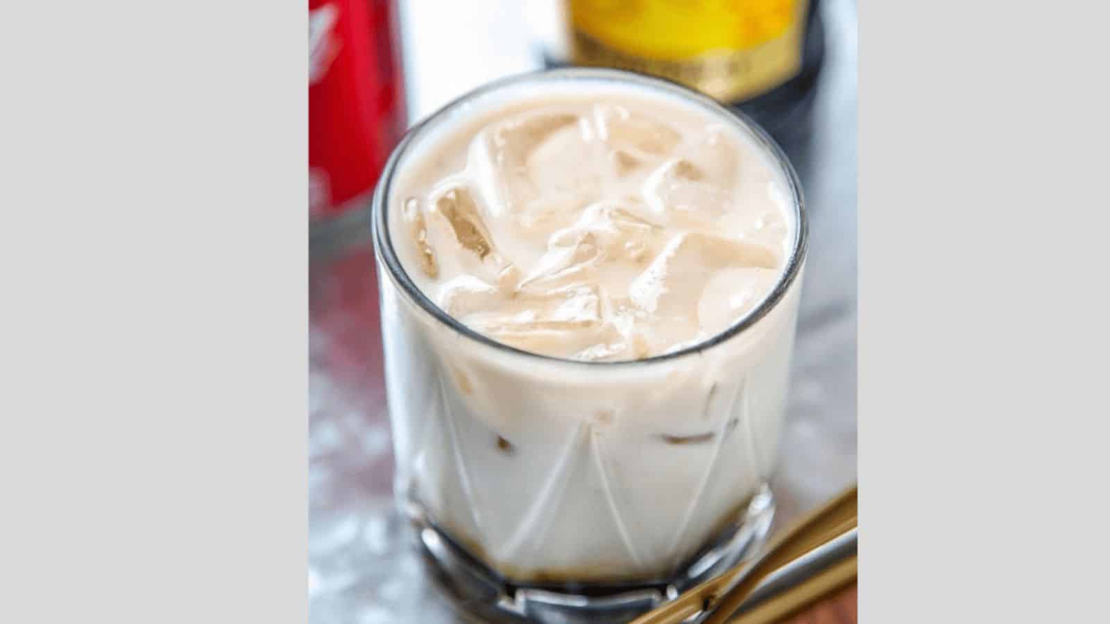 A frothy colorado bulldog with ice in a glass with liquor bottles in the background.