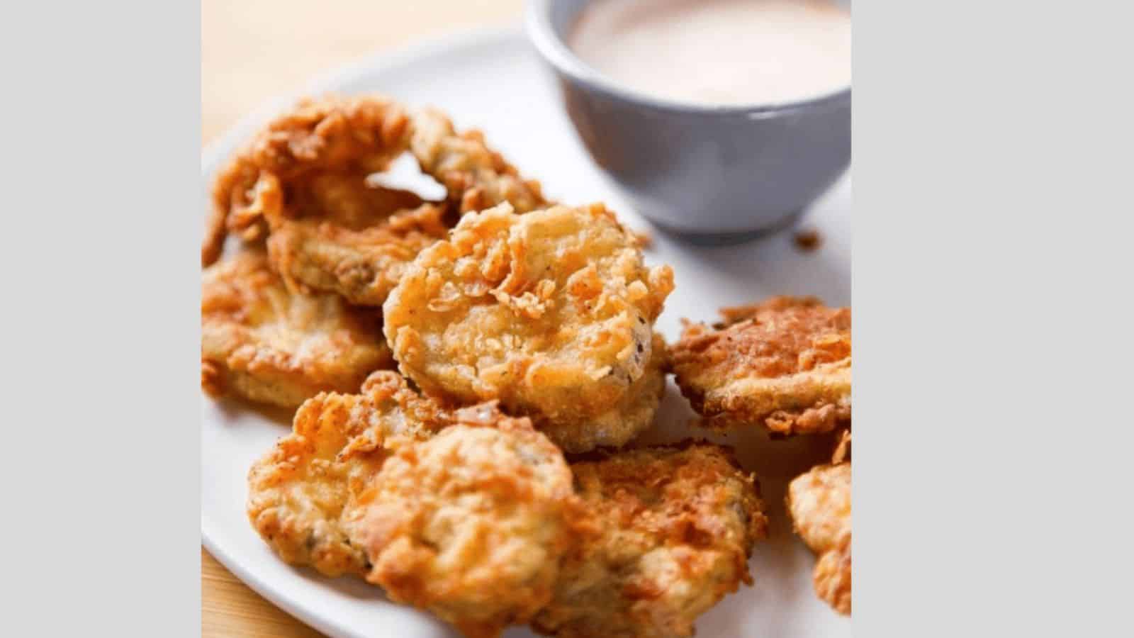 A plate with deep fried pickles and spicy ranch sauce.