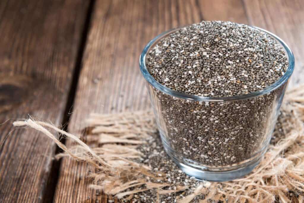 A glass filled with chia seeds on a piece of burlap on a wooden table.