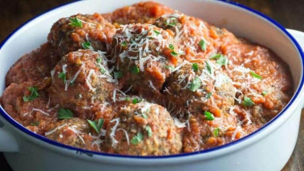 A bowl of meatballs covered in tomato sauce, garnished with grated cheese and chopped parsley.