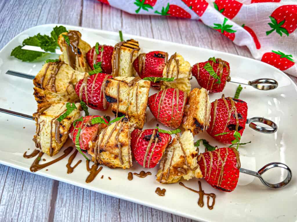 Three pieces of Grilled Strawberry Shortcake Skewers on a white plate.