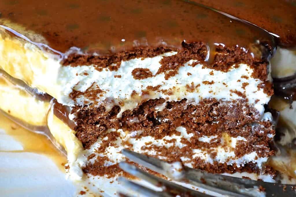 Close-up of a partially eaten layered chocolate and cream cake with visible fork marks and caramel sauce topping.