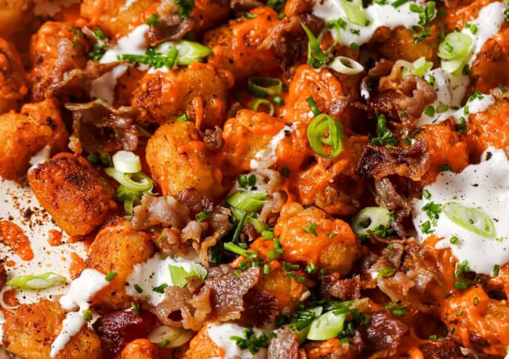 Close-up of loaded tater tots topped with melted cheese, sour cream, green onions, bacon bits, and chopped parsley.