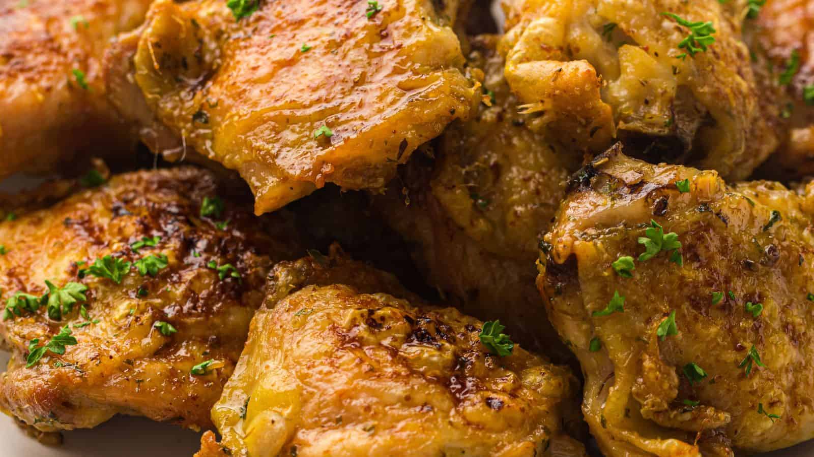 Close-up of cooked chicken thighs, seasoned with herbs and garnished with chopped parsley.