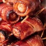 Close-up of a pile of bacon-wrapped sausages held together with toothpicks, showing crispy, browned edges.