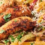 A plate of spaghetti is topped with grilled chicken strips, sliced bell peppers, onions, and garnished with grated cheese and parsley.