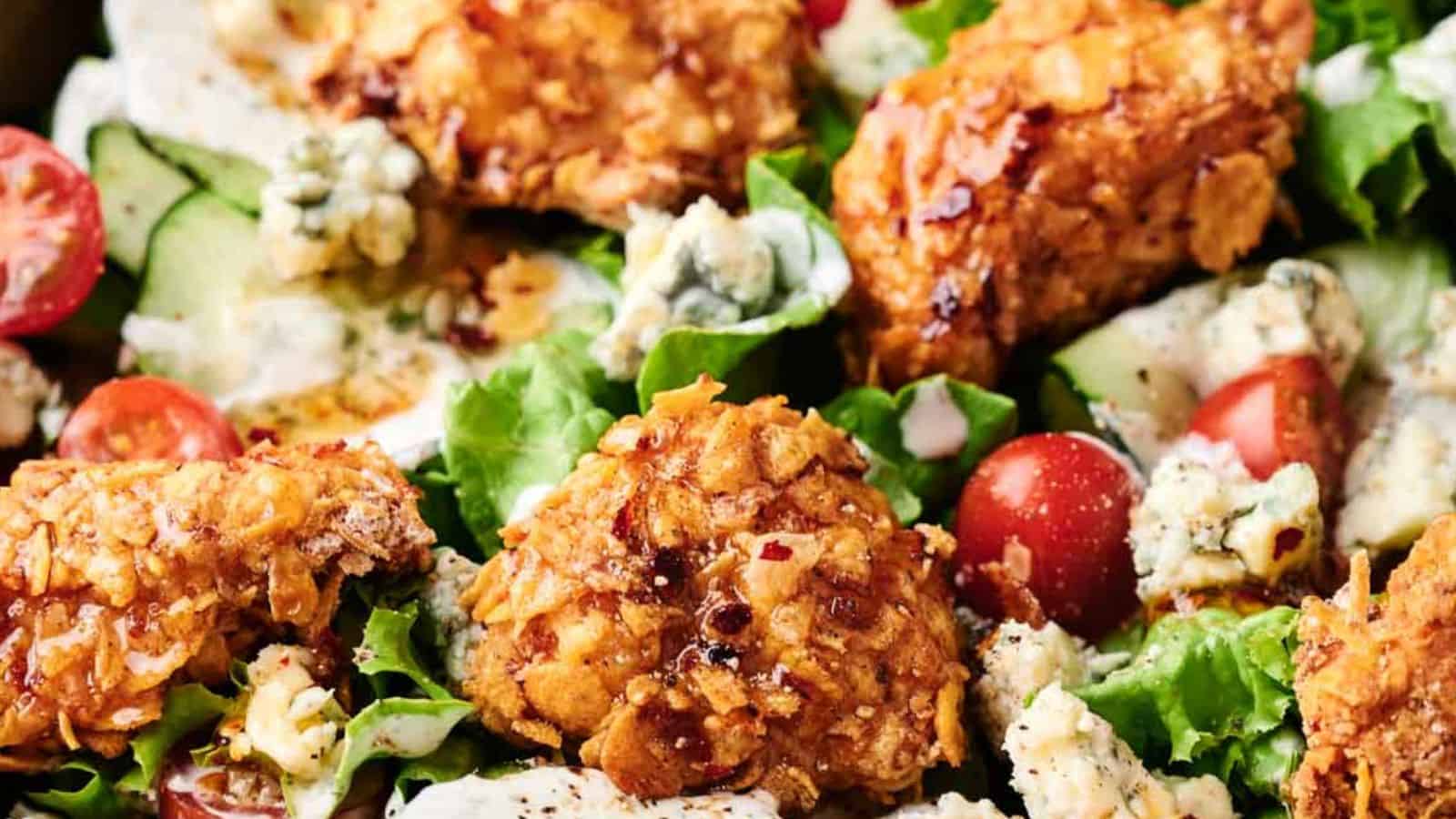 A honey hot chicken salad with succulent fried chicken pieces, cherry tomatoes, blue cheese crumbles, cucumber slices, and mixed greens, all topped with a creamy dressing.