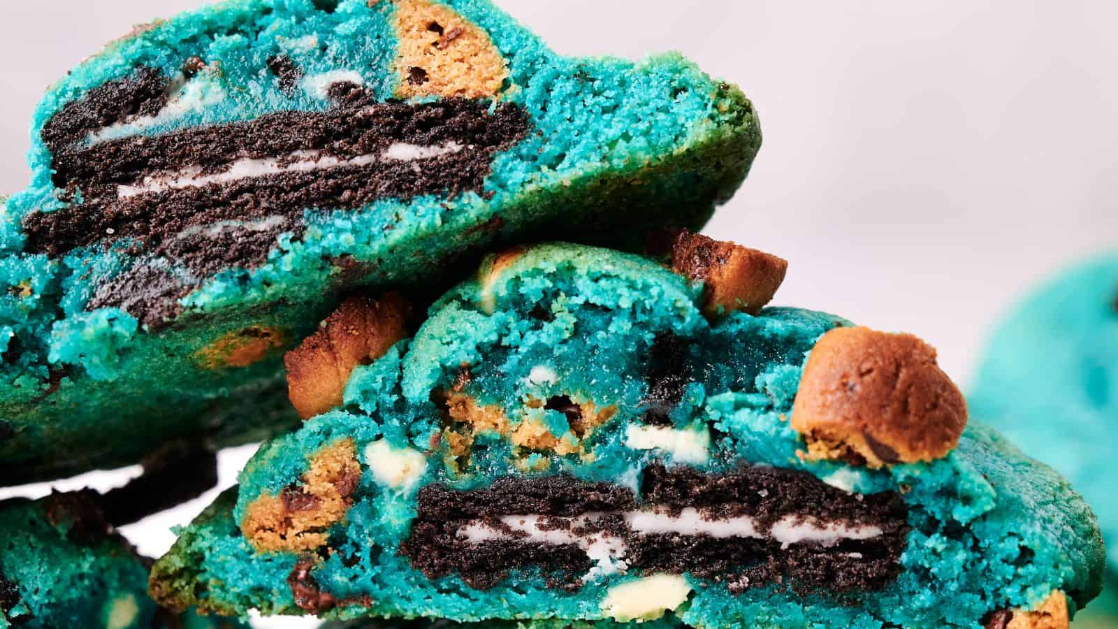 Close-up of a stack of vibrant blue Cookie Monster cookies with Oreo centers and chocolate chips. The cookies are cracked open, revealing the Oreo cookies inside.