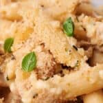 A close-up of a plate of baked penne pasta topped with breadcrumbs, fresh basil leaves, and a creamy sauce with visible chunks of mushrooms and possibly chicken.