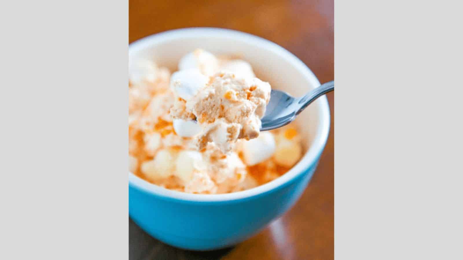 A blue bowl of orange fluff with mandarin orange and mini marshmallows.