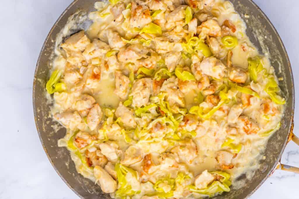 A skillet filled with a creamy chicken and pepper dish, featuring chunks of chicken and green pepper slices in a rich, white sauce.