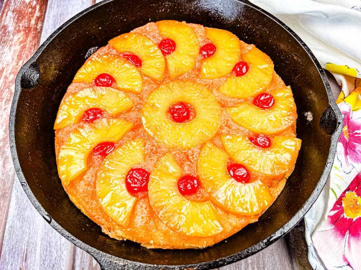 A pineapple upside-down cake with pineapple rings and maraschino cherries in a cast iron skillet.