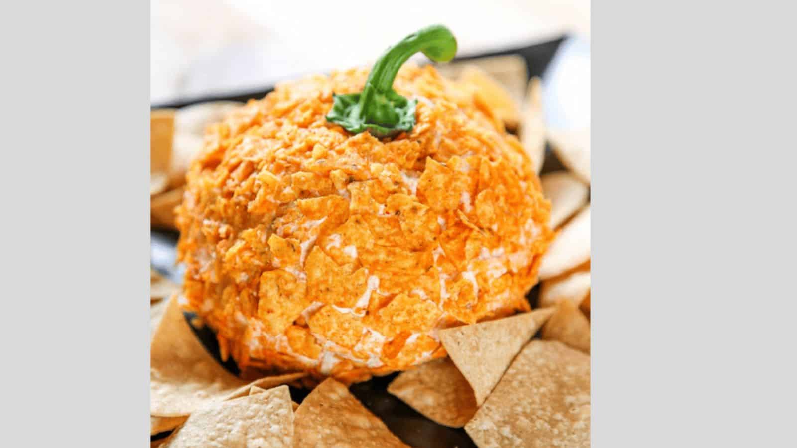 A dorito pumpkin cheeseball topped with a bell pepper stem surrounded by chips.