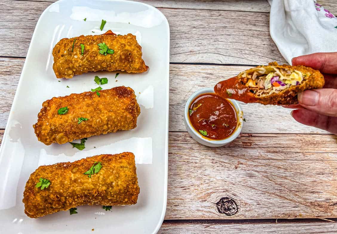 A hand is holding half of the Redneck Eggrolls, with pieces on a white plate.