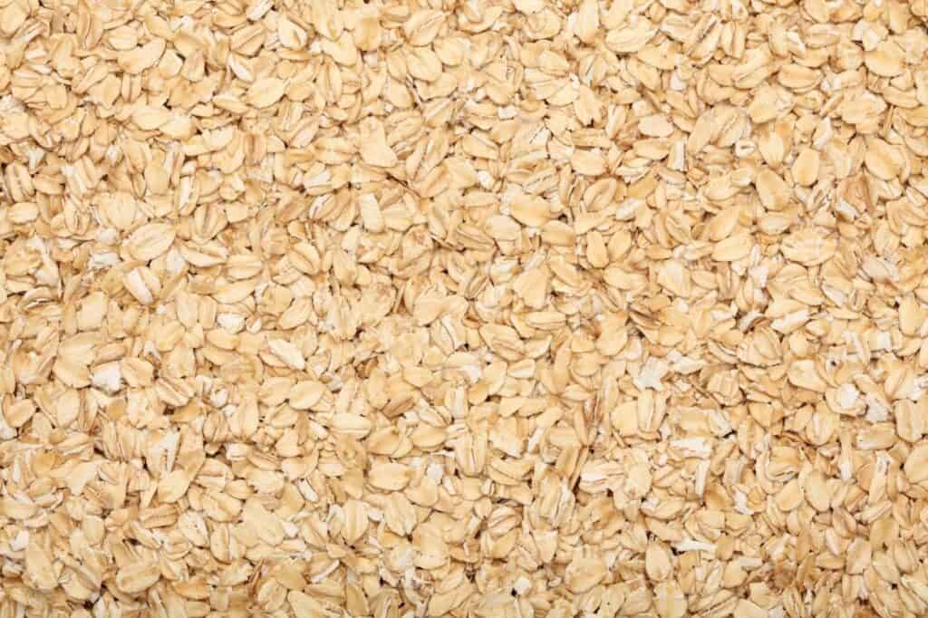 A close-up view of uncooked rolled oats, showcasing their light brown and beige color and flat, oval shape.