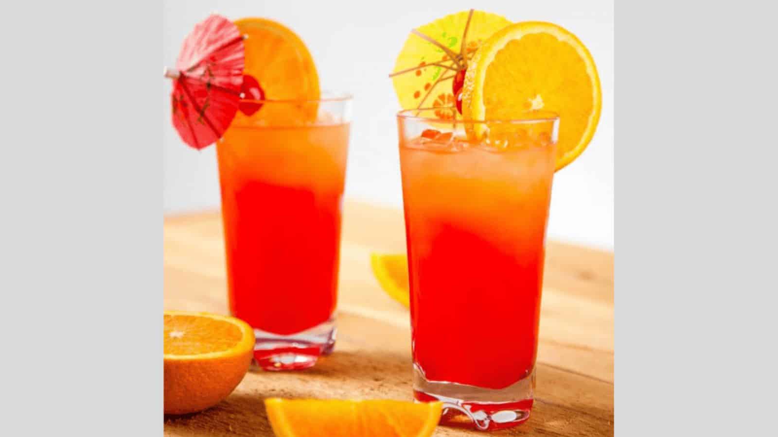 Two layered tequila sunrise drinks topped with a cherry and cocktail umbrella.